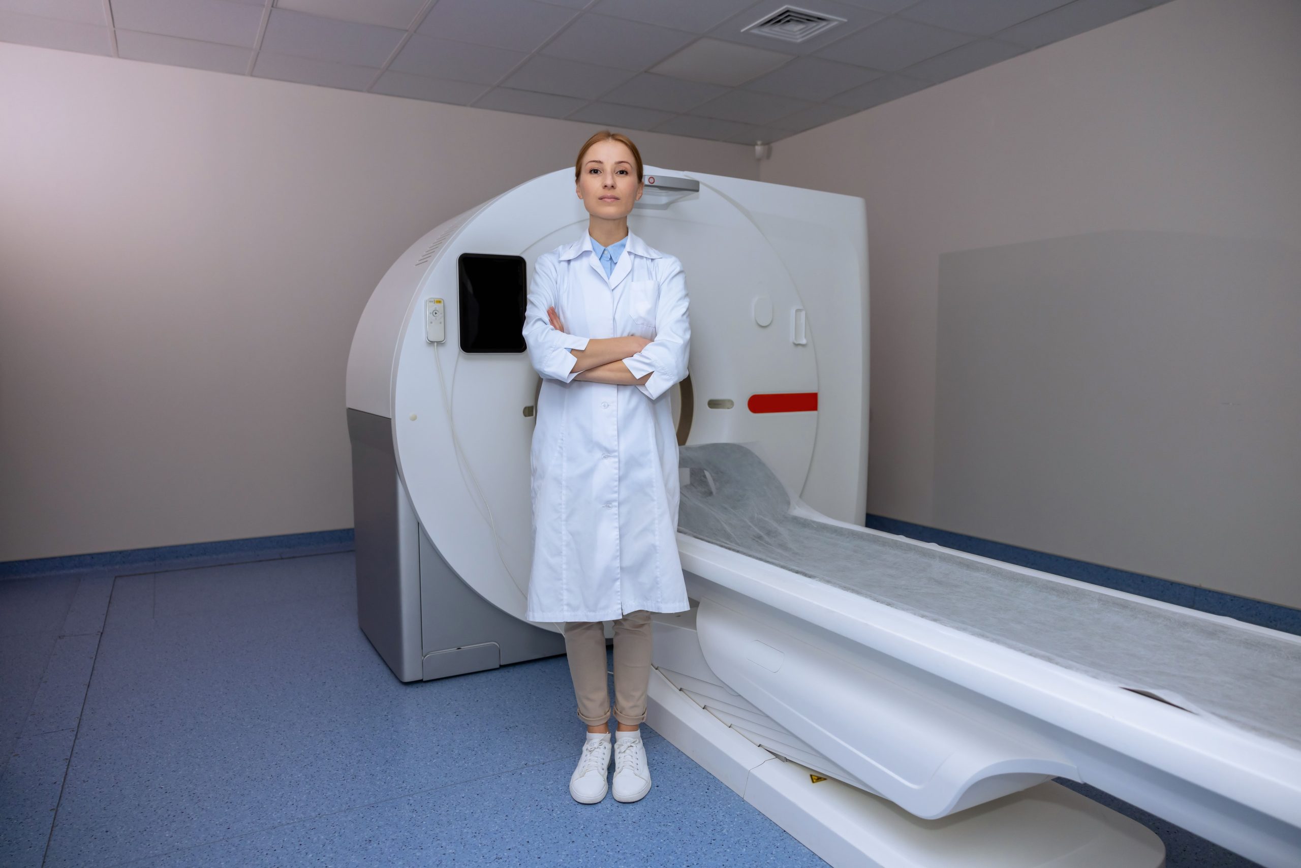 Young Adult Blonde Doctor Standing Near Computed Tomography Scanner Hospital Wearing Lab Coat Smiling Camera Min Scaled